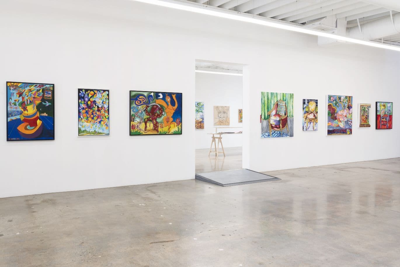 Eine Kunstgalerie mit farbenfrohen Gemälden an weißen Wänden. Eine Tür in der Mitte führt zu einem weiteren Raum mit zusätzlichen Kunstwerken.