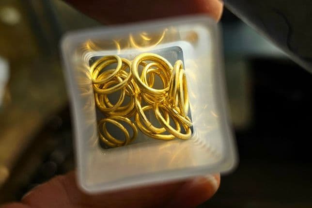 Nahaufnahme einer Person, die einen mit kleinen Goldringen gefüllten Behälter hält, der das Licht reflektiert, von oben gesehen.