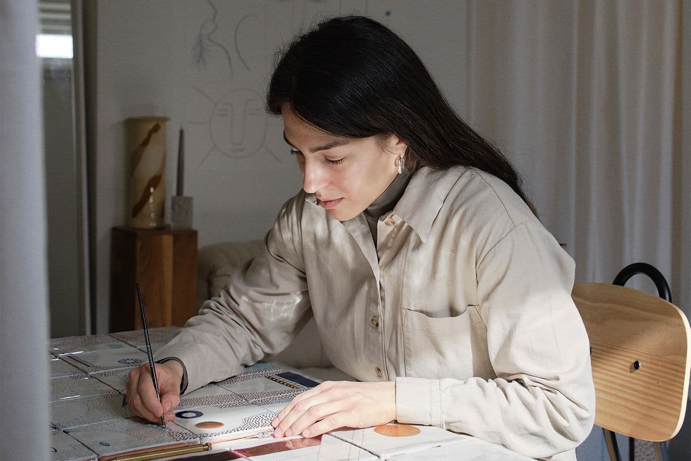 Γυναίκα ζωγραφίζει με λεπτό πινέλο πάνω σε κεραμικά πλακάκια.