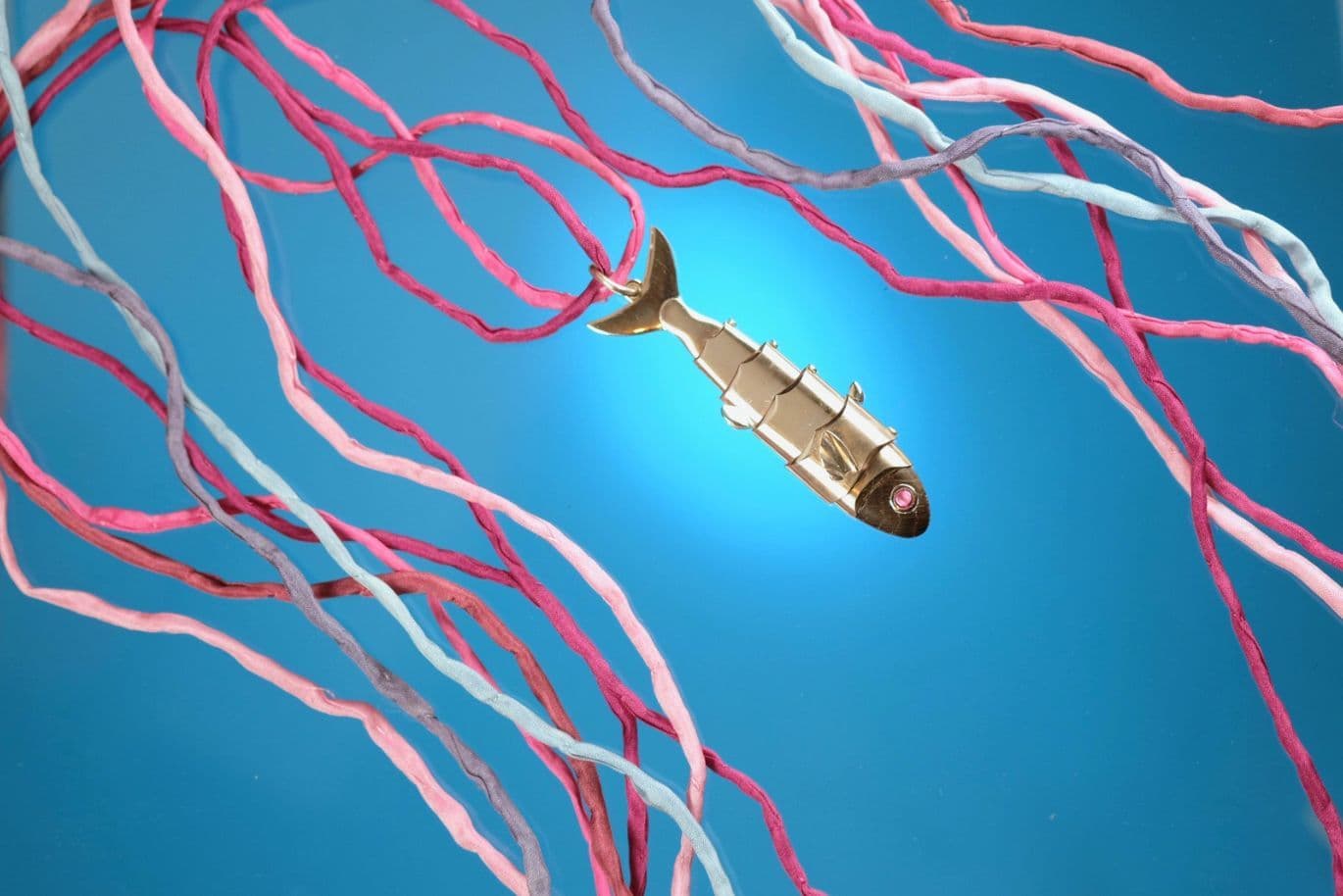 Ein metallischer Fisch schwimmt zwischen leuchtend roten und blauen, verdrehten Bändern vor einem strahlend blauen Hintergrund.