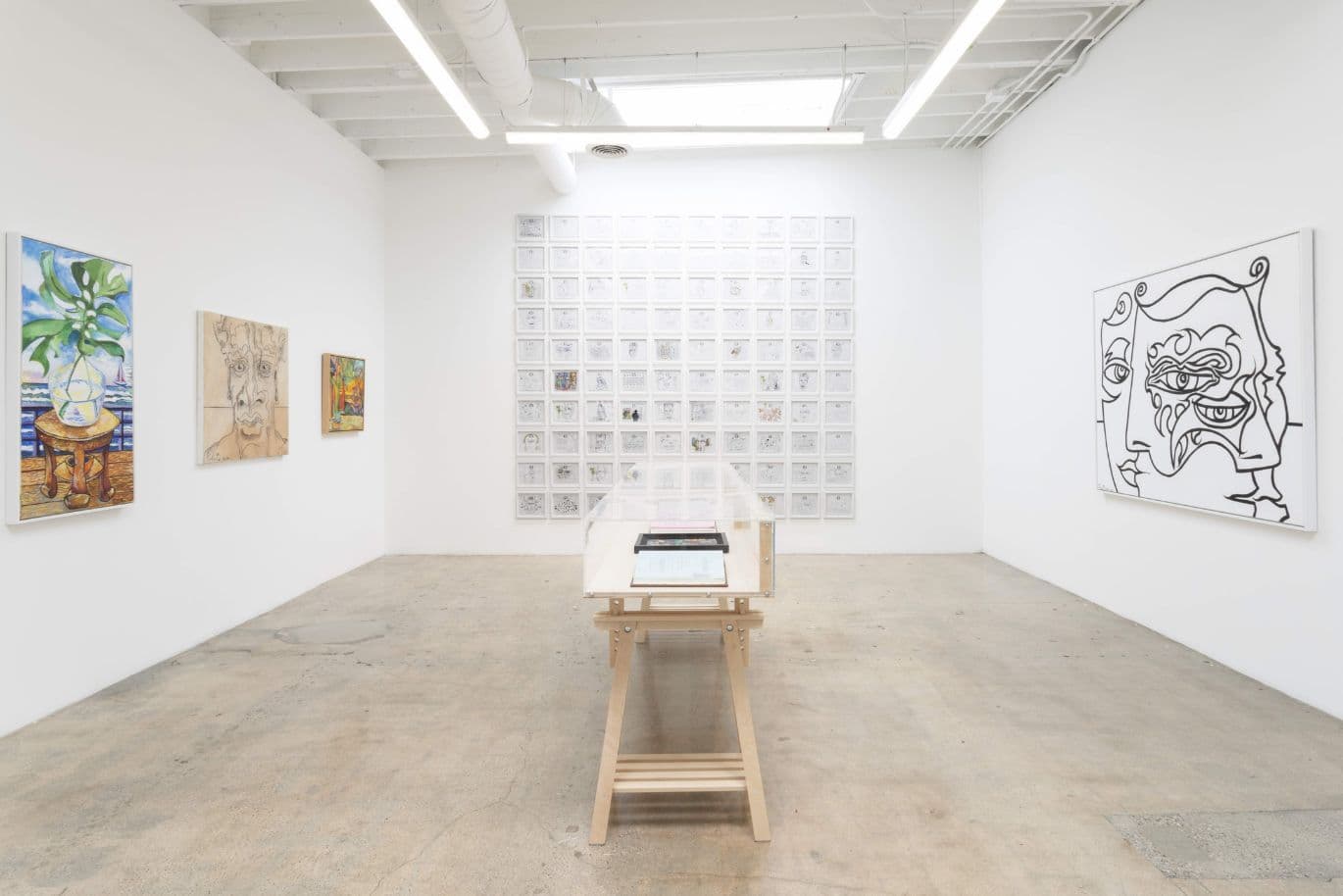 Eine Galerie für moderne Kunst mit abstrakten Gemälden an weißen Wänden und einem Holztisch mit Büchern in der Mitte.