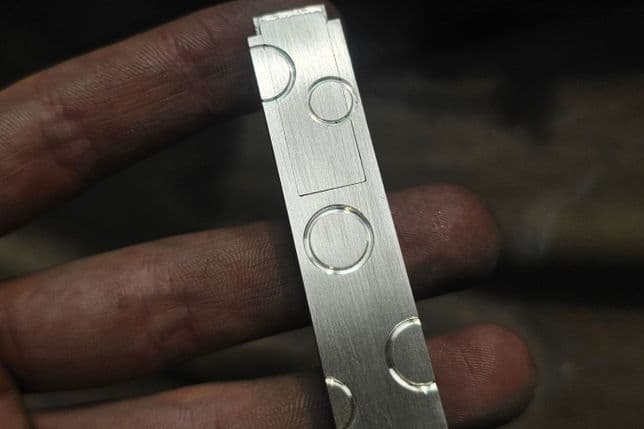 Finger, die eine Lippenstifthülle aus Metalls halten, auf dessen Oberfläche verschiedene kreisförmige Muster eingraviert sind.