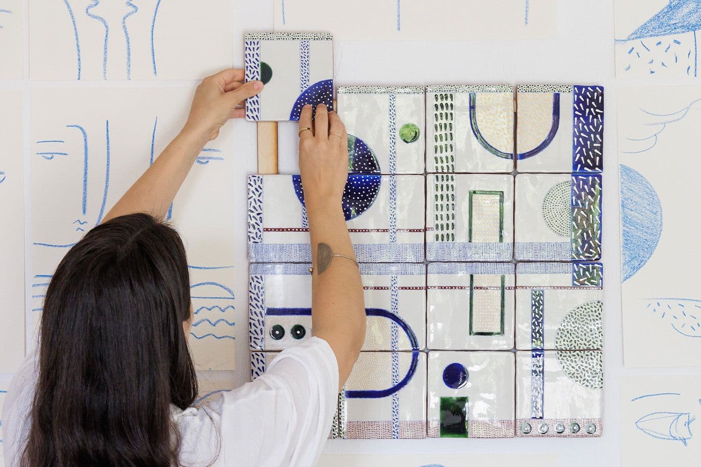 Γυναίκα τοποθετεί κεραμικό πλακίδιο σε καλλιτεχνική σύνθεση στον τοίχο.