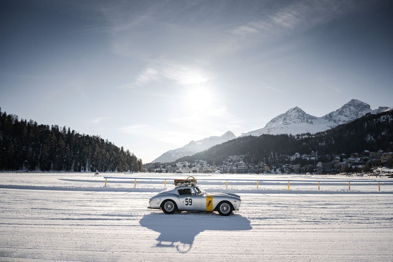 Vintage car racing on a snowy track with mountains in the background, under a clear sky. Car number 59 with a yellow accent.