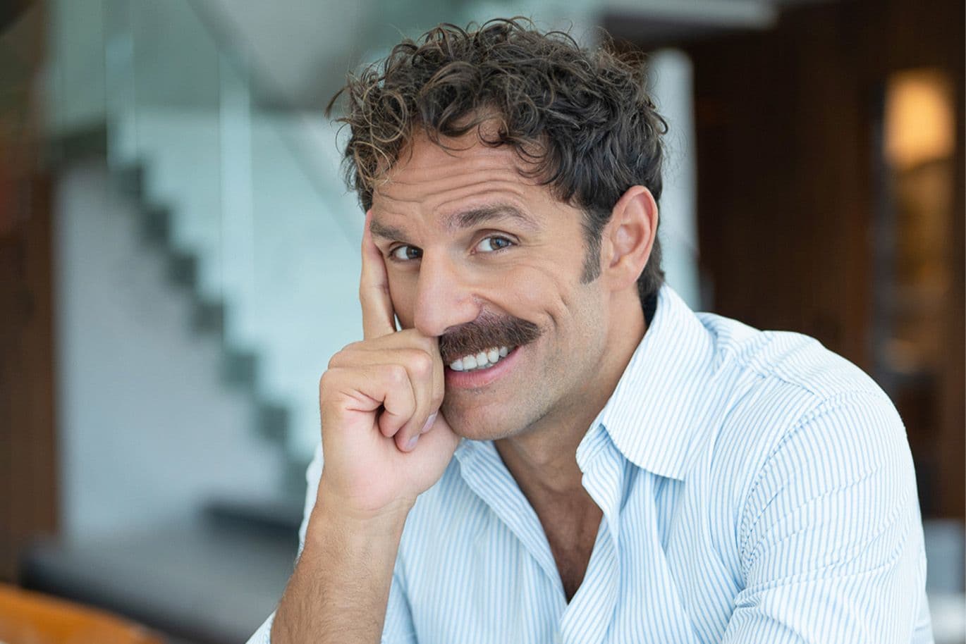 Άνδρας με λευκό κοστούμι, κάθεται και χαμογελάει στην κάμερα