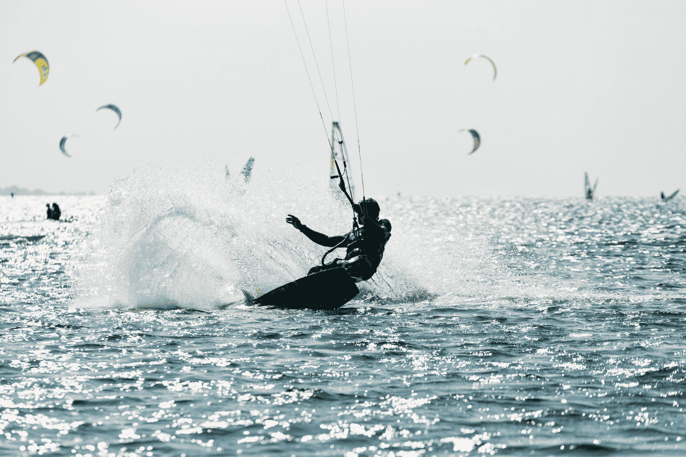 A kite surfer glides swiftly over the water, pulled by a colorful kite against the bright sky. Waves splash around as the rider skillfully maneuvers across the sea, full of energy and freedom.