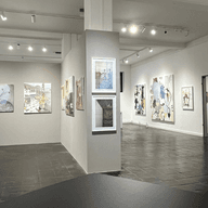 Galerie mit weißen Wänden und Bildern an der Wand, eine Trennwand in der Mitte ermöglicht weitere Bilder aufzuhängen