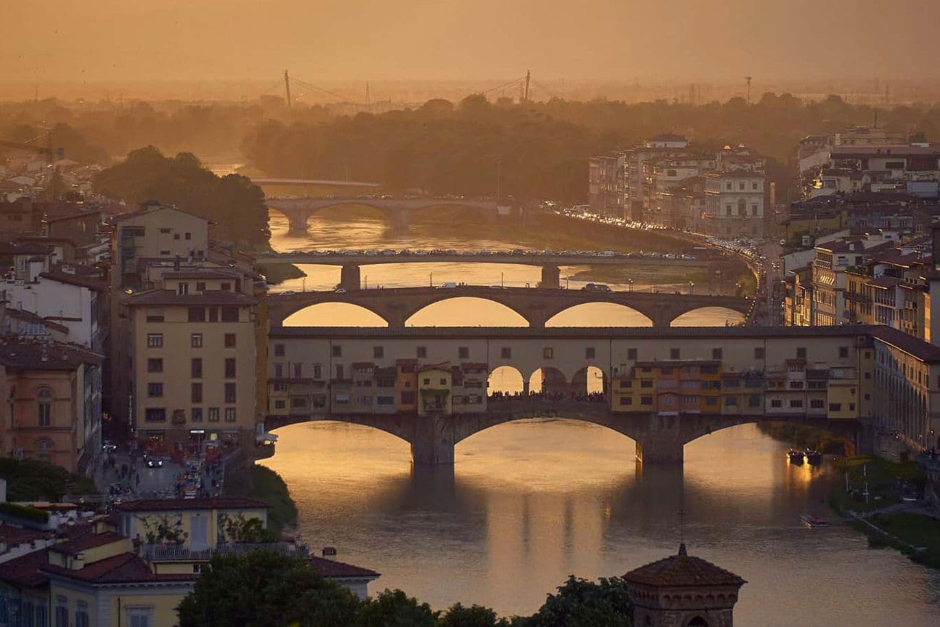Coucher de soleil sur le Ponte Vecchio à Florence, en Italie, avec une lumière chaude qui se reflète sur l'Arno et les bâtiments historiques environnants.