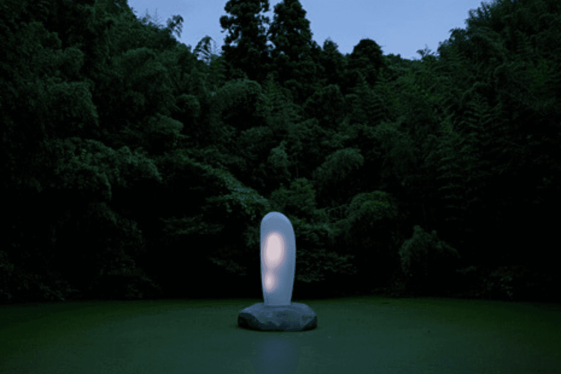 Eine leuchtende abstrakte Skulptur auf einem Felsen in einem stillen, dunkelgrünen Wald in der Abenddämmerung.