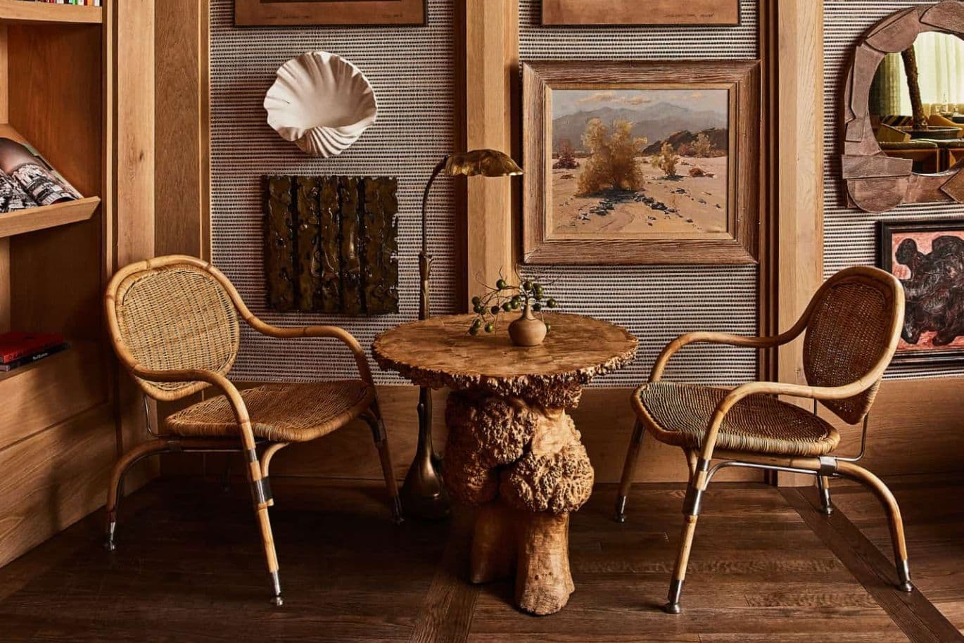 Ein gemütlicher Raum mit einem rustikalen Holztisch, zwei Korbstühlen, gerahmten Bildern an den Wänden und einer kleinen Pflanze auf dem Tisch. Warme, erdige Farbtöne prägen den Raum.