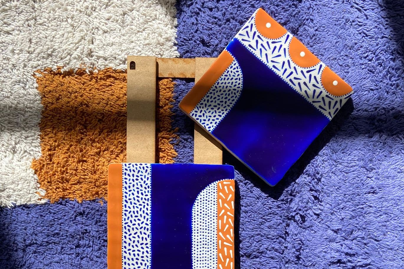 Δύο κεραμικά πλακίδια με μπλε, λευκά και πορτοκαλί μοτίβα πάνω σε πολύχρωμο χαλί.