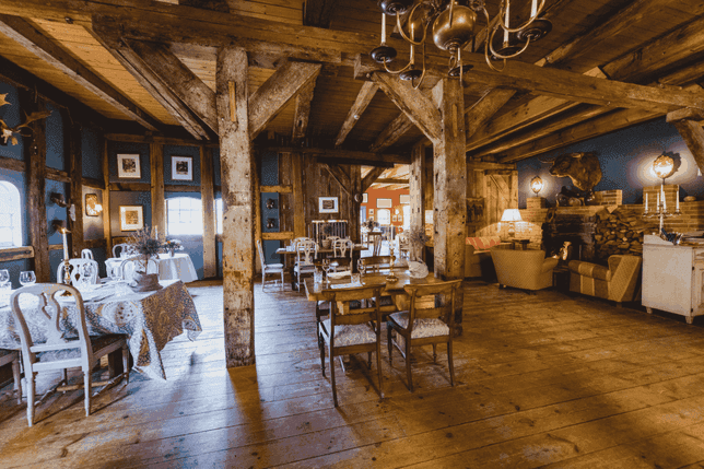 Rustic dining area with wooden beams, vintage furniture, and warm lighting. Tables are set for dining, and a cozy seating area is visible.