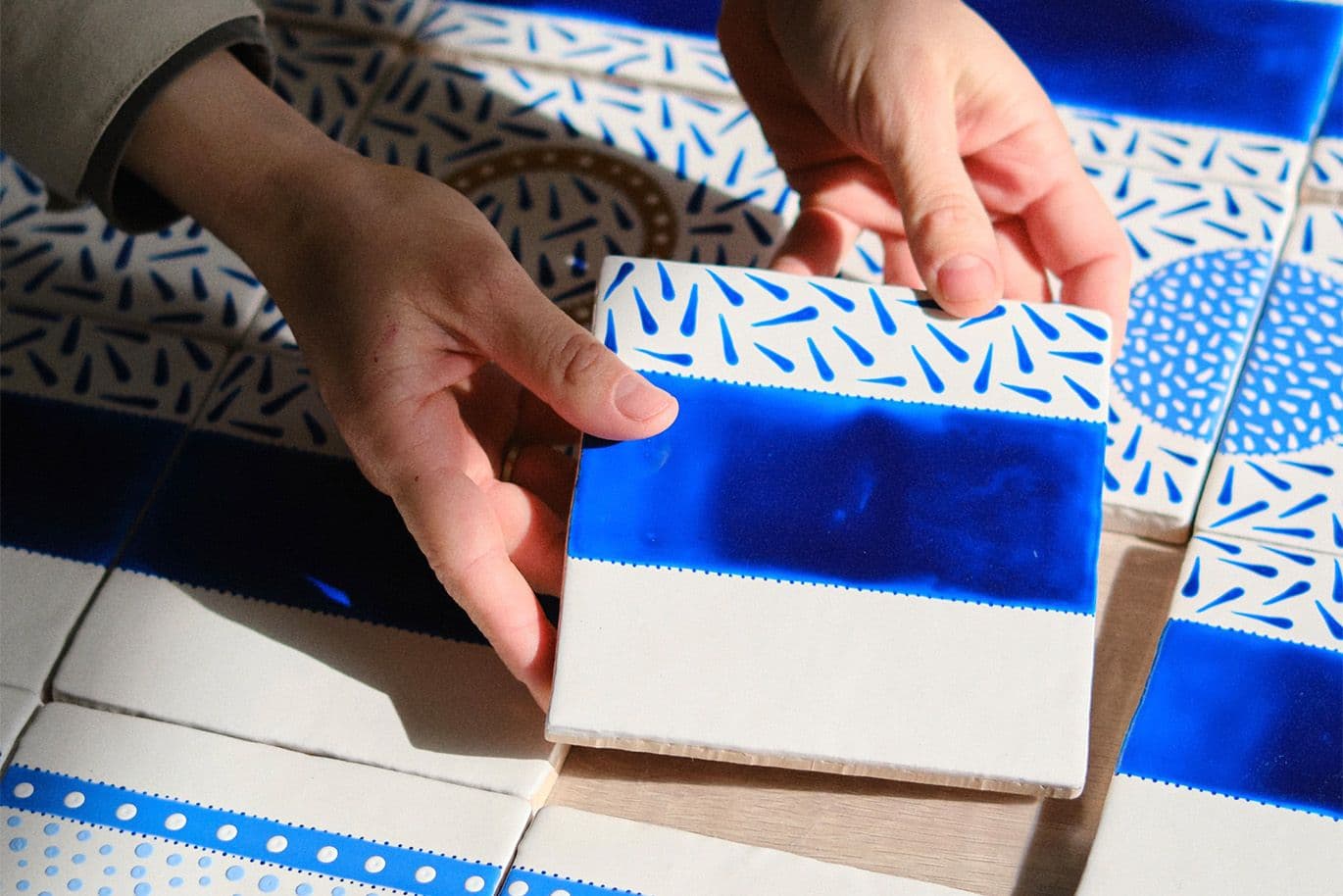 Χέρια κρατούν διακοσμητικό κεραμικό πλακίδιο με μπλε σχέδια.