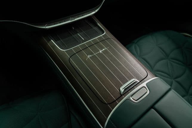 Innenraum des Fahrzeugs mit luxuriöser, holzverkleideter Mittelkonsole mit charakteristischer Gravur und gesteppten grünen Ledersitzen.