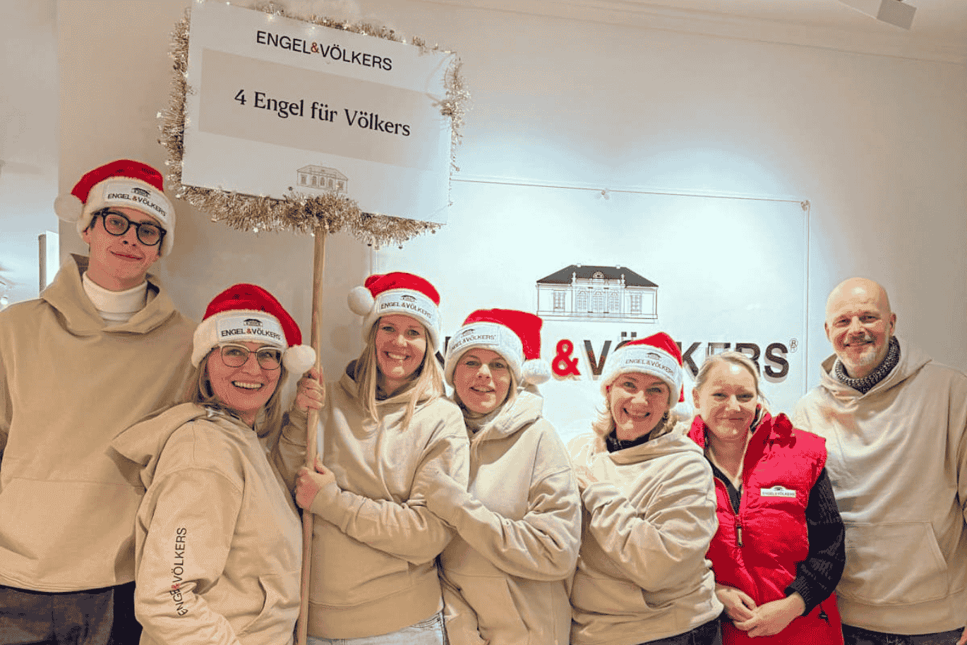 team of 6 people all in beige hoodies, wearing red christmas hats