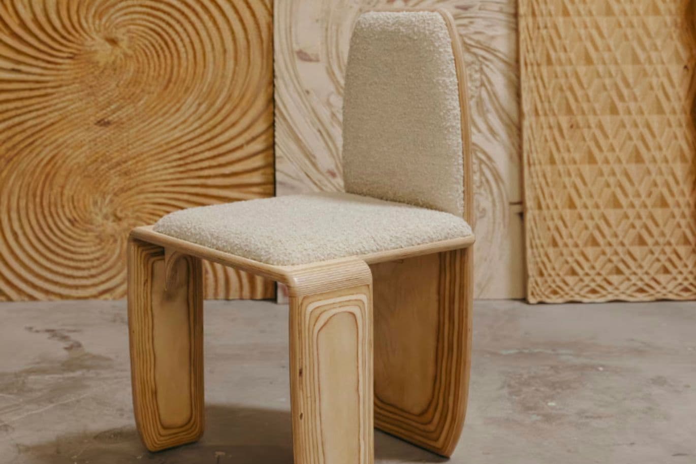 Ein moderner Stuhl mit strukturierter, beiger Sitzfläche und Rückenlehne sowie geschwungenen Holzbeinen, der vor dem Hintergrund gemusterter Holzpaneele steht.
