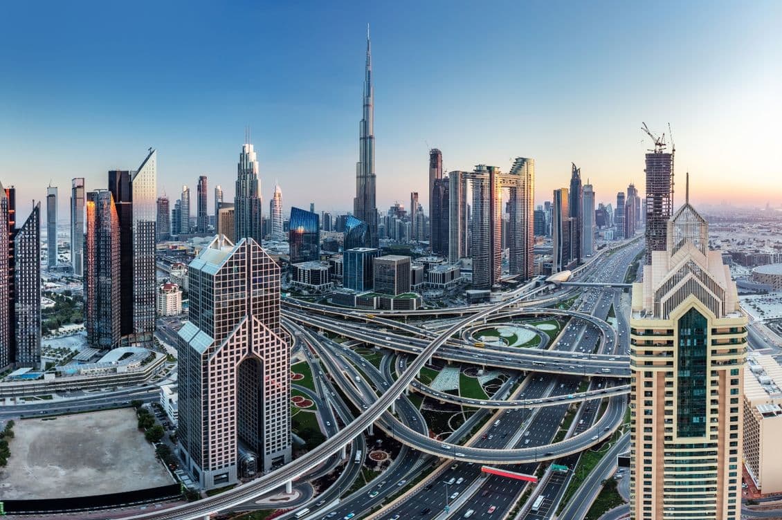 Dubai skyline at sunset. Tall buildings and skyscrapers, including the Burj Khalifa, rise above a complex highway system.