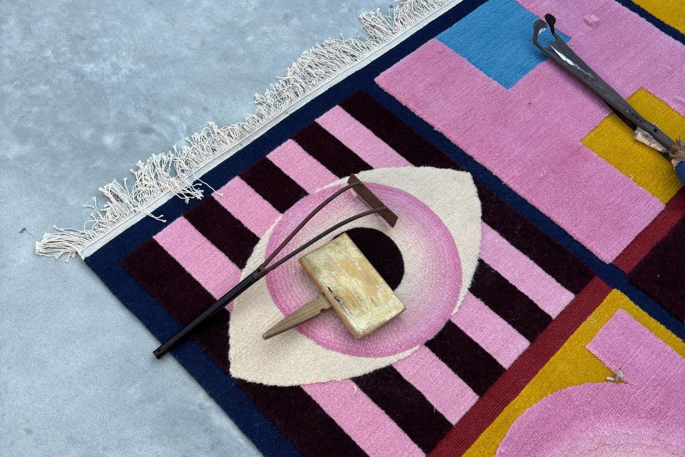 Colorful geometric rug with eye design on the floor, a small wooden block, and a metal tool placed on top.
