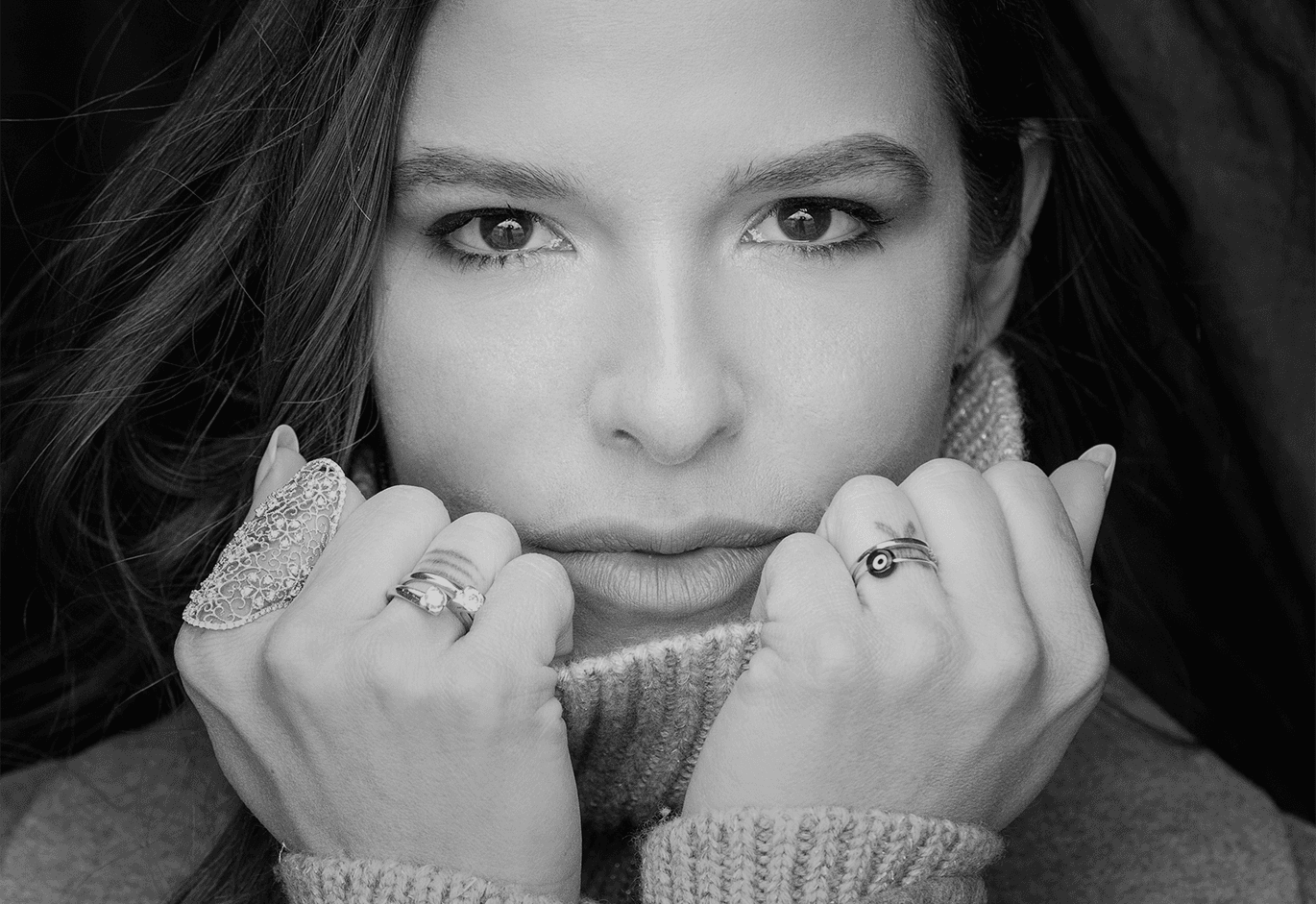 Ασπρόμαυρο κοντινό πορτρέτο γυναίκας με κοσμήματα και πλεκτό ζιβάγκο που καλύπτει το στόμα.