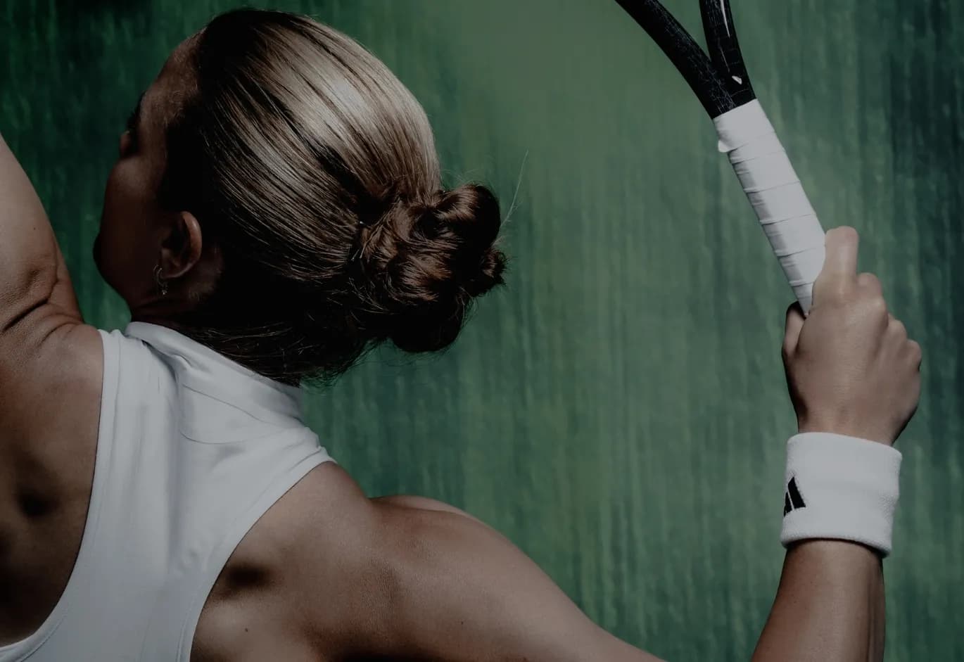 Back view portrait of tennis player Maria Sakkari holding a racket over her shoulder in a white athletic top.