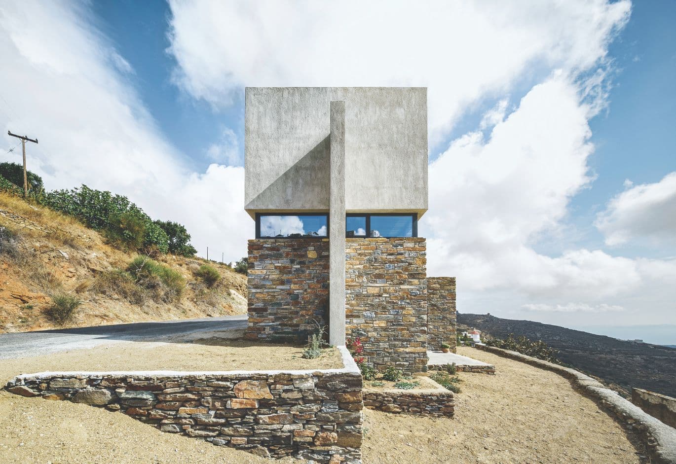 Minimalist stone and concrete house on a hillside with panoramic views under a blue sky