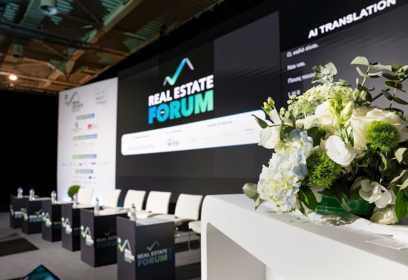 Real Estate Forum conference stage setup with floral arrangements, presentation screen, and panel seating