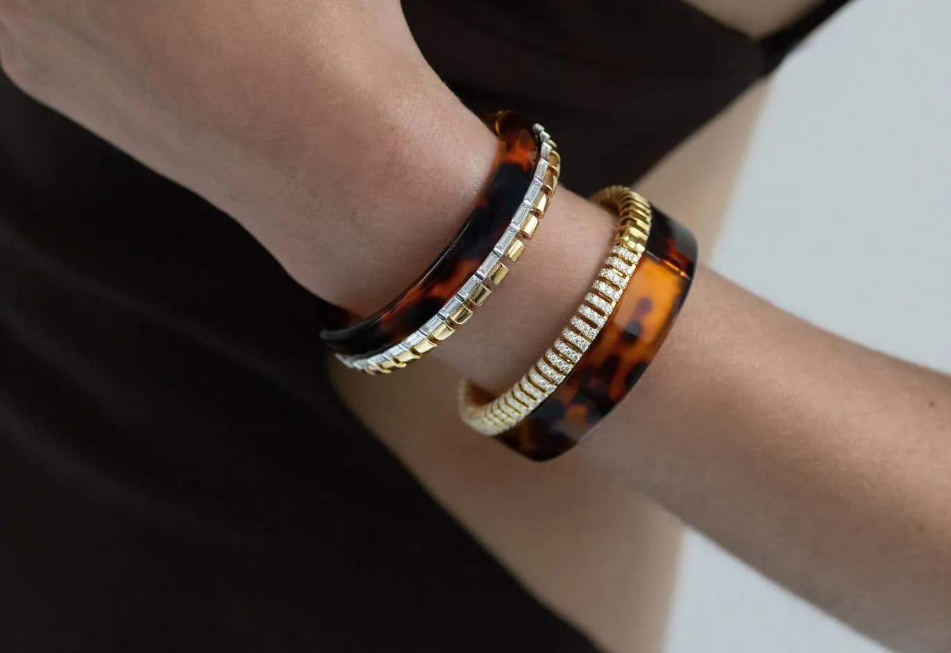 Close-up of a woman's wrist wearing two tortoiseshell bangles set with gold and diamonds.