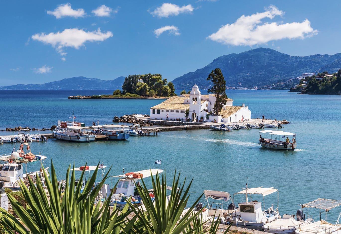 Small seaside church on an islet with boats, turquoise waters, and mountain backdrop