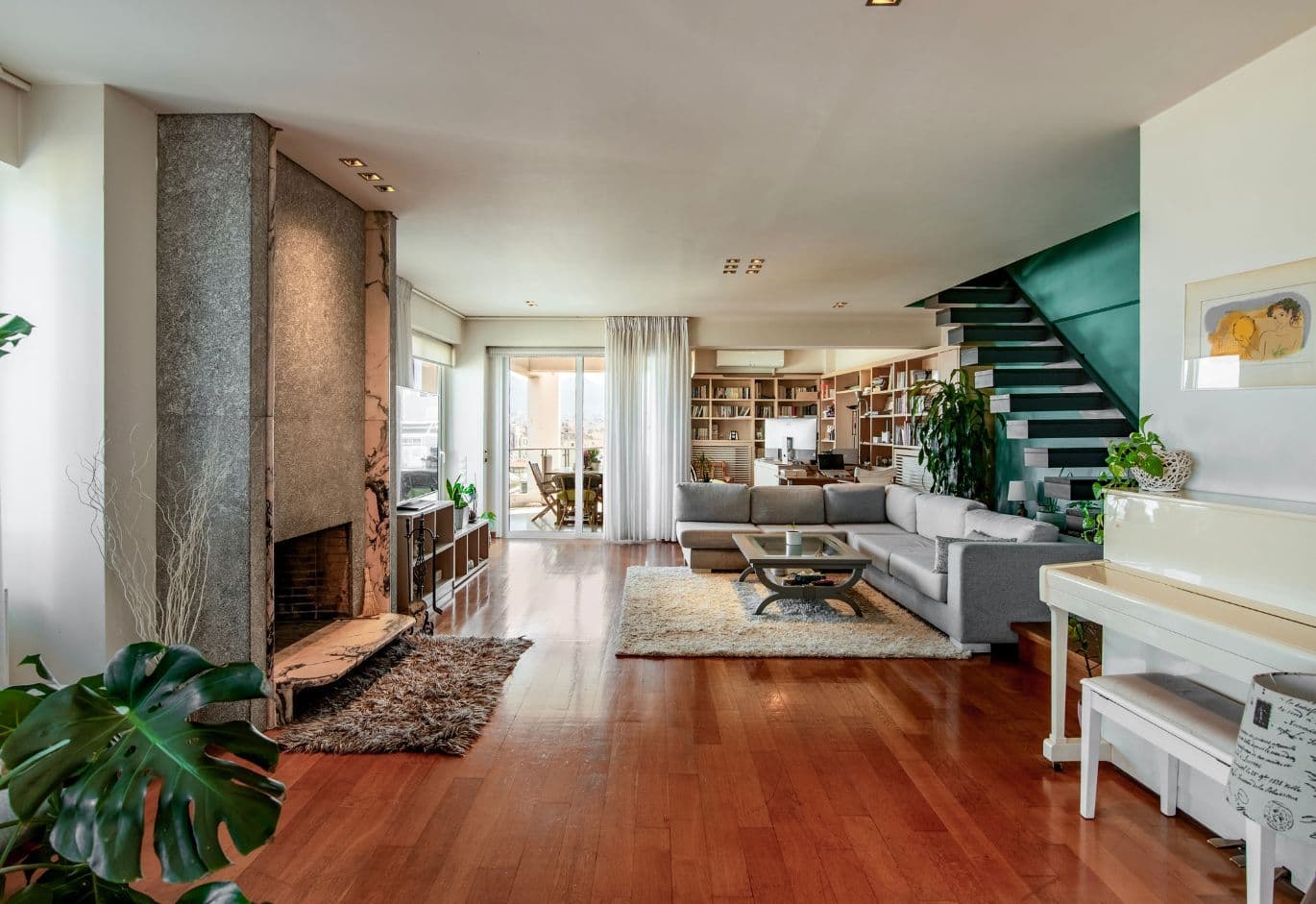 Modern living room with fireplace, wooden floors, staircase, and open-plan layout with natural light