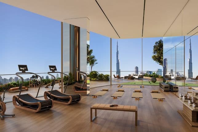 Modern gym with treadmills, yoga mats, and weights overlooking a city skyline and a tall tower through floor-to-ceiling windows.