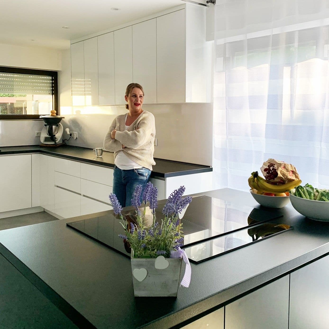 Bright, modern kitchen with a central cooking island, white cabinets and a woman standing relaxed by the counter