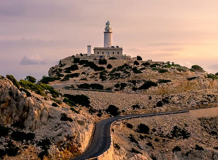 Lighthouse atop a rocky cliff at sunset.