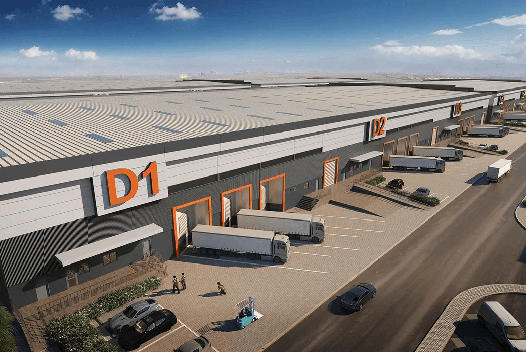 Aerial view of a large industrial warehouse complex with multiple loading docks, trucks, and parking areas, under a clear blue sky.