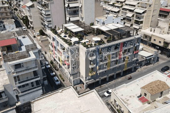 Luftaufnahme eines modernen Wohngebäudes mit Dachterrasse, umgeben von Straßen und anderen Gebäuden.