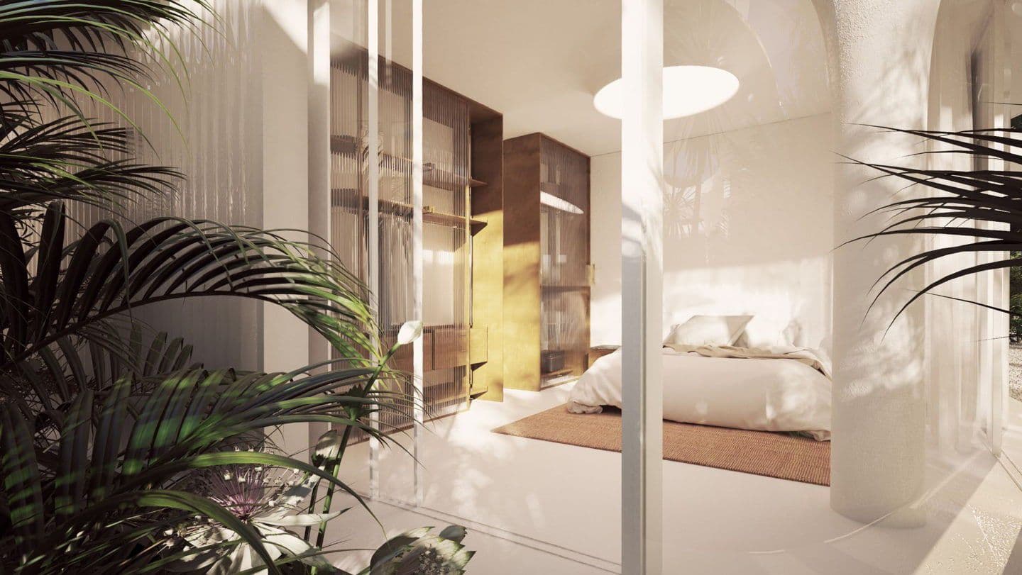 Bright bedroom with white walls, a bed, and a brown rug. A wooden closet is visible. Green plants are in the foreground.