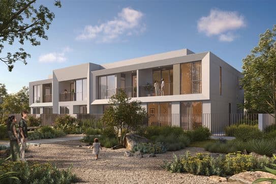 Modernes zweistöckiges Haus mit großen Fenstern, umgeben von einem angelegten Garten. Im Vordergrund geht eine Familie auf einem Kiesweg spazieren.