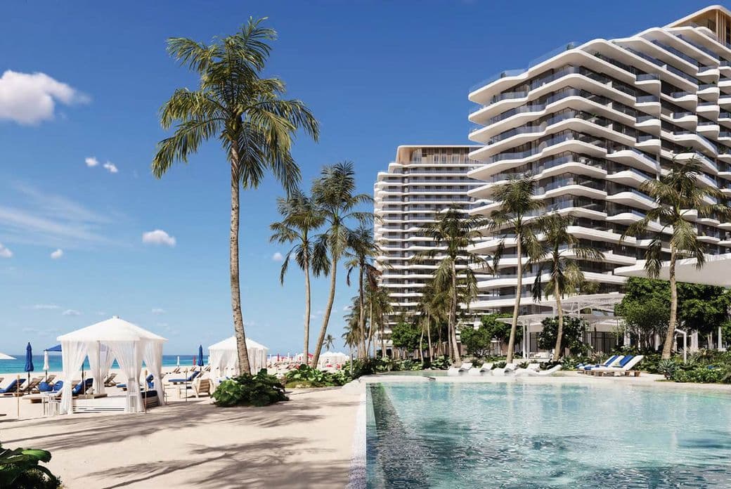 Beachfront resort with modern high-rise buildings, palm trees, a clear swimming pool, and cabanas, overlooking a sandy beach and blue ocean.