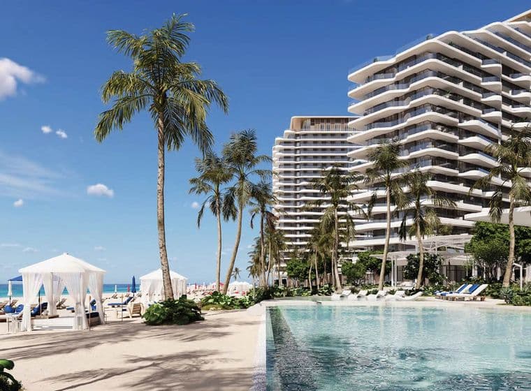 Beachfront resort with modern high-rise buildings, palm trees, a clear swimming pool, and cabanas, overlooking a sandy beach and blue ocean.