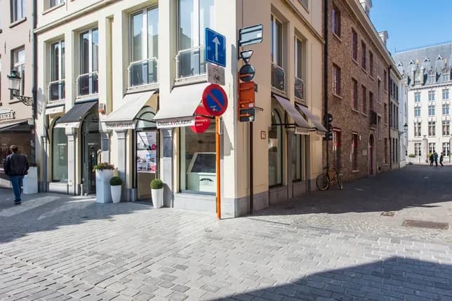 Street corner with modern buildings, large windows, and a no-entry sign. Cobblestone pavement and a bicycle parked near the entrance.