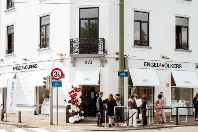 People standing outside a white Engel & Völkers building with large windows and a balloon decoration near the entrance.