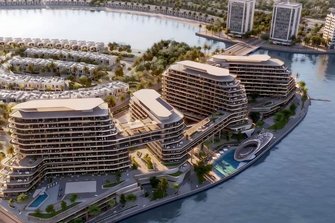 Aerial view of modern waterfront buildings with curved architecture, surrounded by water and greenery, under a clear sky.