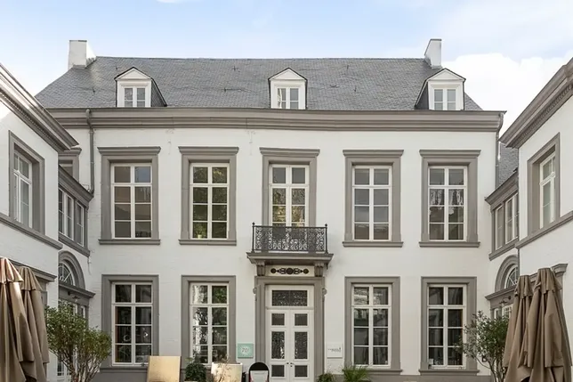 A symmetrical, white building with tall windows and a central entrance. It features a small balcony and a sloped roof with dormer windows.