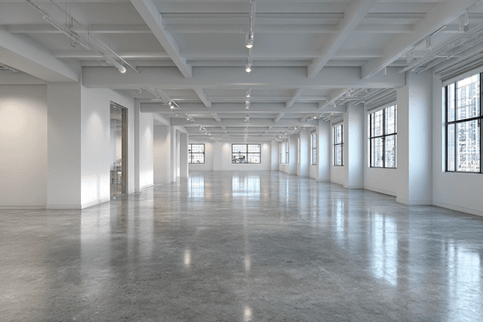 Spacious empty room with polished concrete floor, white walls, large windows, and ceiling lights, overlooking cityscape buildings.