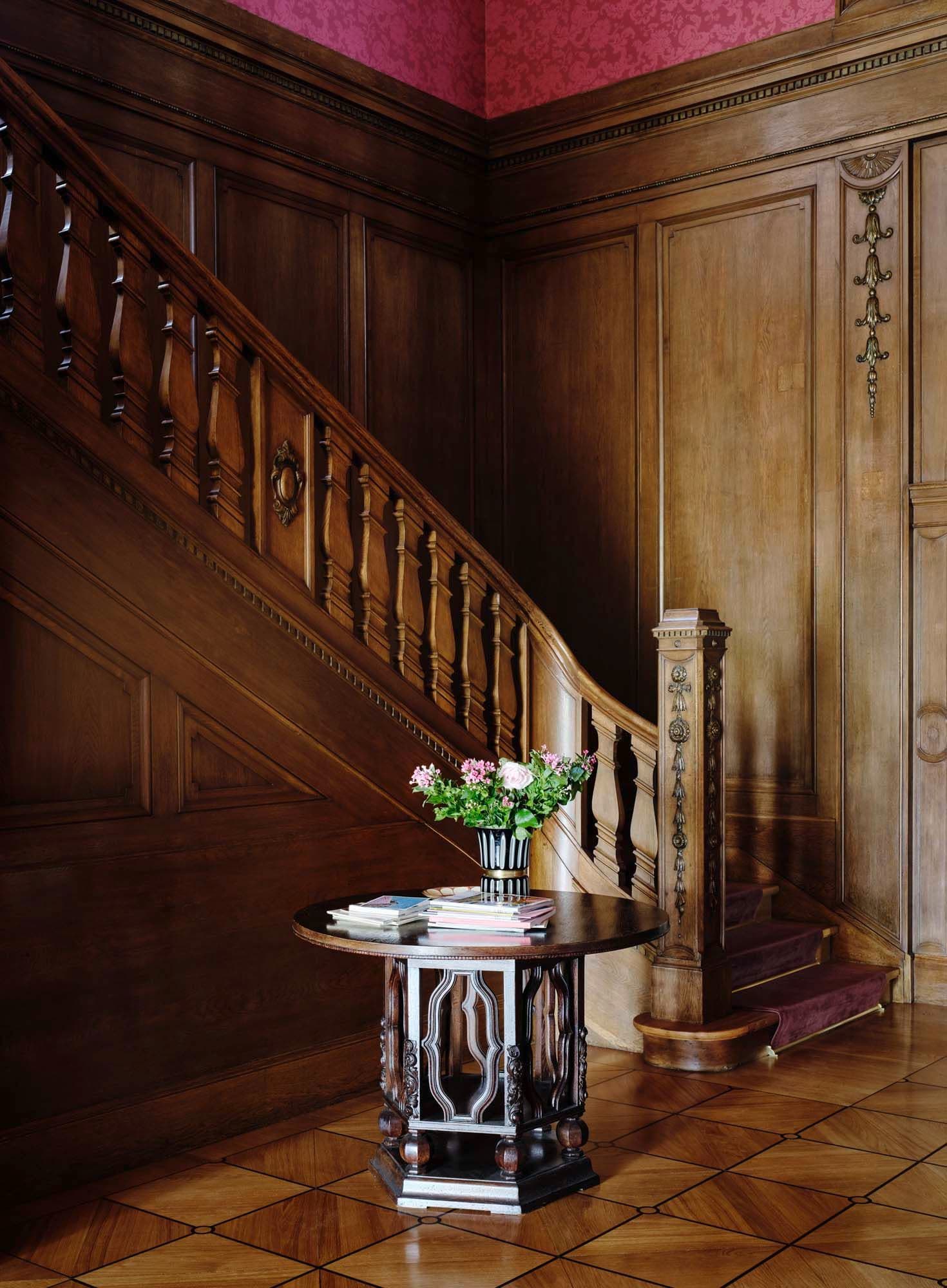 A foyer with wood paneled walls, a staircase, and a round table with a vase of flowers.