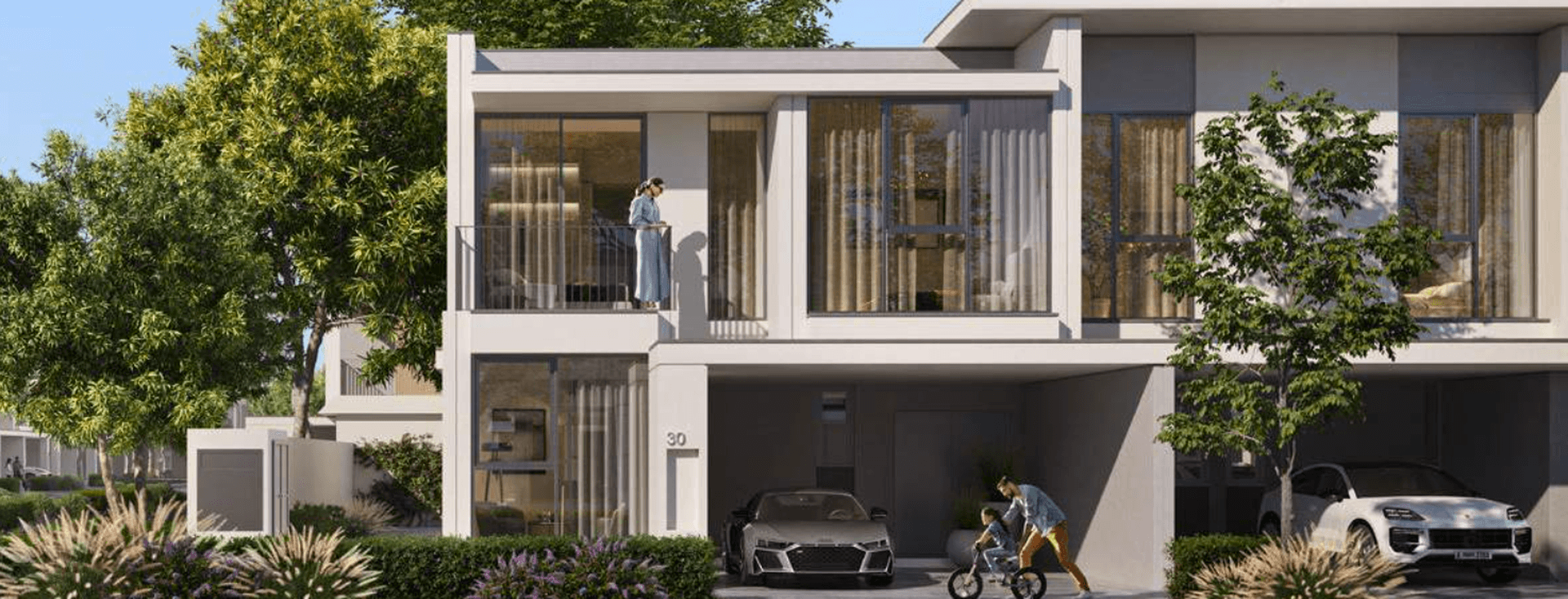 A modern townhouse exterior at Vindera at The Valley featuring large windows, private parking, landscaped greenery, and residents enjoying the outdoor space.