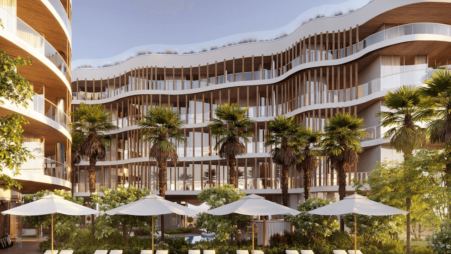 Modern building with wavy balconies, palm trees, and poolside loungers under umbrellas, set in a sunny, landscaped area.