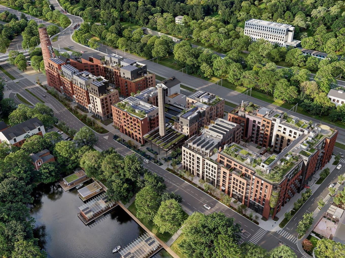 Letecký pohled na rozsáhlý rezidenční komplex s cihlovými budovami a zelenými střechami, zasazený mezi ulicí, lesoparkem a řekou s přístavištěm.