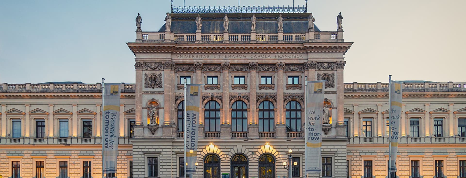 Neoklassizistisches Universitätsgebäude mit verzierter Steinfassade, Statuen entlang der Dachlinie, Bogenfenstern und Schriftbändern