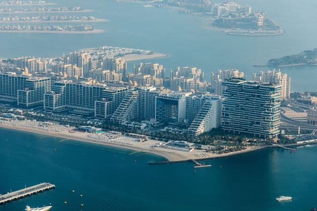 Aerial view of West Beach, Palm Jumeirah with modern buildings, beaches, and waterfront, featuring a cluster of high-rise structures and palm-shaped islands.