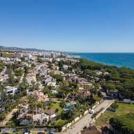 Luftaufnahme der Golden Mile, die Villen und Wohnungen zeigt, umgeben von grünen Pflanzen neben dem blauen Meer.